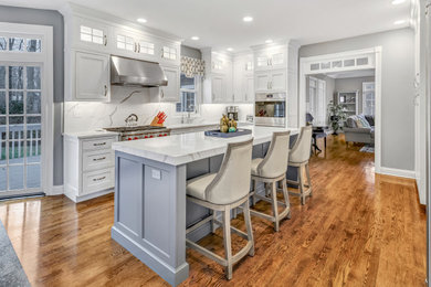 This is an example of a traditional kitchen in New York with white cabinets, engineered stone countertops, an island, engineered quartz splashback, integrated appliances and medium hardwood flooring.