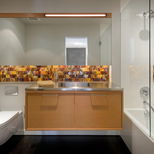 Inspiration for a mid-sized contemporary master orange tile and glass tile dark wood floor and black floor bathroom remodel in Portland with furniture-like cabinets, medium tone wood cabinets, a wall-mount toilet, white walls, an integrated sink, stainless steel countertops and a hinged shower door