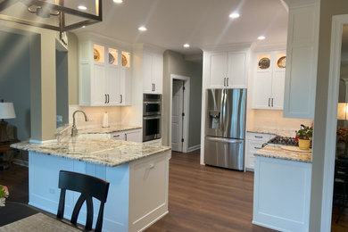 Large minimalist l-shaped laminate floor and brown floor eat-in kitchen photo in Chicago with a farmhouse sink, shaker cabinets, white cabinets, quartz countertops, white backsplash, ceramic backsplash, stainless steel appliances, a peninsula and multicolored countertops