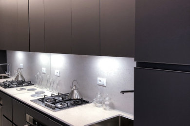 Ispirazione per una piccola cucina minimalista con lavello a vasca singola, ante lisce, ante nere, paraspruzzi bianco, pavimento in legno verniciato e top bianco