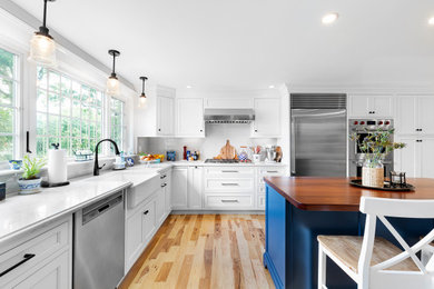 Foto de cocina comedor tradicional con fregadero sobremueble, salpicadero blanco, electrodomésticos de acero inoxidable, suelo de madera clara, una isla y encimeras blancas