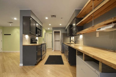 Example of a small minimalist galley light wood floor and beige floor open concept kitchen design in Austin with an undermount sink, recessed-panel cabinets, black cabinets, wood countertops, white backsplash, porcelain backsplash, stainless steel appliances, no island and beige countertops