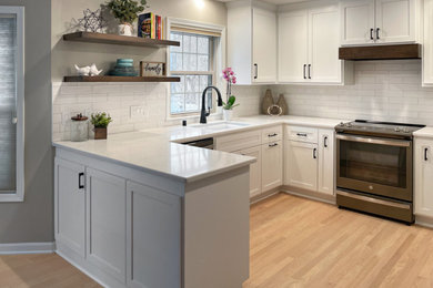 Medium sized traditional l-shaped kitchen/diner in Milwaukee with a submerged sink, shaker cabinets, white cabinets, engineered stone countertops, white splashback, porcelain splashback, stainless steel appliances, light hardwood flooring, a breakfast bar, beige floors and white worktops.