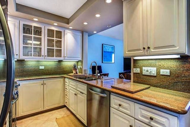 Photo of a beach style kitchen in Hawaii with an undermount sink, raised-panel cabinets, white cabinets, granite benchtops, multi-coloured splashback, stone slab splashback, stainless steel appliances, travertine floors and no island.