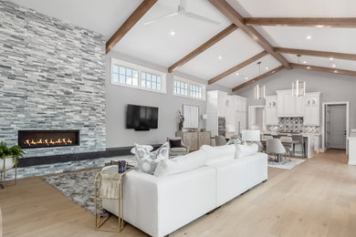Imagen de salón abierto y abovedado moderno extra grande con paredes grises, suelo de madera clara, piedra de revestimiento, televisor colgado en la pared y suelo beige