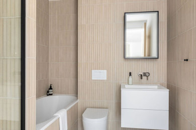 Inspiration for a medium sized modern cream and black ensuite bathroom in London with flat-panel cabinets, white cabinets, a built-in bath, an alcove shower, a wall mounted toilet, beige tiles, porcelain tiles, beige walls, porcelain flooring, an integrated sink, beige floors, a hinged door, white worktops, a single sink and a floating vanity unit.