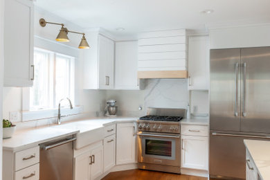 Example of a large transitional l-shaped medium tone wood floor eat-in kitchen design in Detroit with a farmhouse sink, shaker cabinets, white cabinets, quartz countertops, white backsplash, quartz backsplash, stainless steel appliances, an island and white countertops