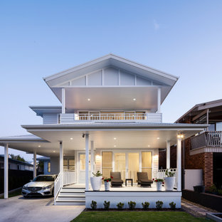 This is an example of a large beach style two-storey white house exterior in Sydney with concrete fiberboard siding, a gable roof, a metal roof, a white roof and board and batten siding.