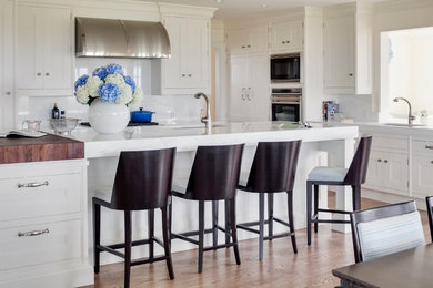 Eat-in kitchen - large contemporary l-shaped medium tone wood floor and brown floor eat-in kitchen idea in Boston with an undermount sink, recessed-panel cabinets, white cabinets, marble countertops, white backsplash, stone slab backsplash, stainless steel appliances and an island