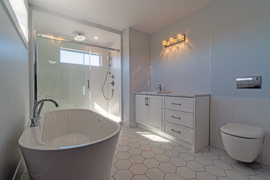 Photo of a mid-sized transitional bathroom in Other with shaker cabinets, white cabinets, an alcove tub, a shower/bathtub combo, a wall-mount toilet, white walls, ceramic floors, a trough sink, white floor, a sliding shower screen, grey benchtops, a double vanity and a built-in vanity.