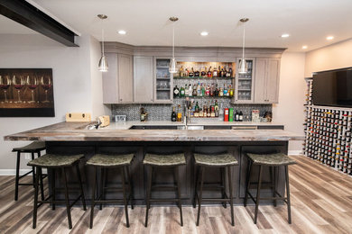 Small urban u-shaped vinyl floor and brown floor seated home bar photo in DC Metro with an undermount sink, shaker cabinets, medium tone wood cabinets, quartz countertops, gray backsplash, metal backsplash and gray countertops
