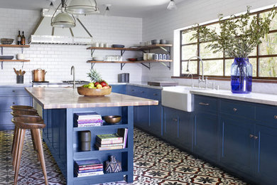 Photo of a transitional l-shaped kitchen in Los Angeles with blue cabinets, white splashback, with island, concrete floors, a farmhouse sink, shaker cabinets and subway tile splashback.