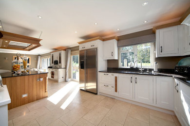 This is an example of an expansive traditional l-shaped open plan kitchen in London with raised-panel cabinets, white cabinets and with island.