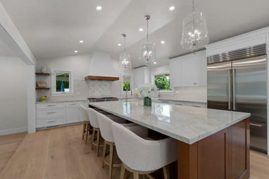Open concept kitchen - large transitional l-shaped light wood floor, beige floor and vaulted ceiling open concept kitchen idea in San Francisco with a farmhouse sink, shaker cabinets, white cabinets, quartzite countertops, multicolored backsplash, porcelain backsplash, stainless steel appliances, an island and multicolored countertops