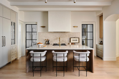 Kitchen - transitional l-shaped light wood floor, beige floor and exposed beam kitchen idea in Austin with a farmhouse sink, shaker cabinets, beige cabinets, beige backsplash, stone slab backsplash, stainless steel appliances, an island and beige countertops