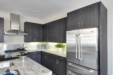 Example of a large transitional l-shaped medium tone wood floor kitchen pantry design in Phoenix with flat-panel cabinets, gray cabinets, white backsplash, glass tile backsplash, stainless steel appliances, an island, an undermount sink and granite countertops