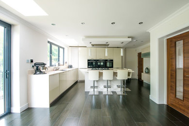 Design ideas for a contemporary l-shaped open plan kitchen in London with a drop-in sink, glass-front cabinets, white cabinets, quartzite benchtops, black appliances, porcelain floors and with island.