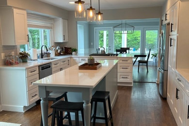 Bild på ett stort lantligt vit vitt kök, med en enkel diskho, släta luckor, vita skåp, bänkskiva i kvarts, blått stänkskydd, stänkskydd i porslinskakel, rostfria vitvaror, mellanmörkt trägolv, en köksö och brunt golv
