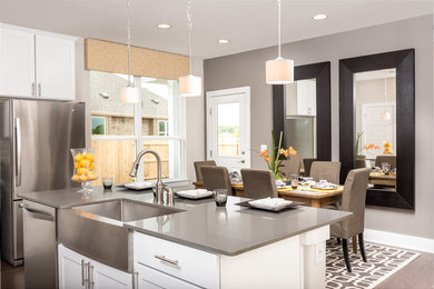 Example of a mid-sized trendy l-shaped light wood floor open concept kitchen design in Austin with an island, a farmhouse sink, white cabinets, quartz countertops, white backsplash, glass tile backsplash, stainless steel appliances and shaker cabinets