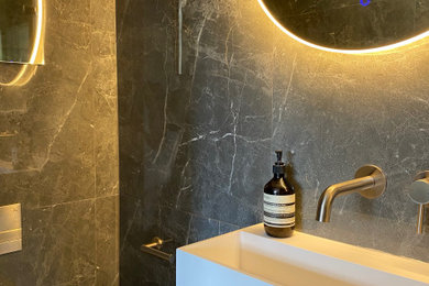 Photo of a small contemporary ensuite bathroom in London with an alcove shower, a one-piece toilet, grey tiles, porcelain tiles, porcelain flooring, a wall-mounted sink, grey floors, a hinged door, feature lighting and a single sink.