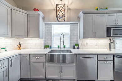 Open concept kitchen - large transitional l-shaped porcelain tile and gray floor open concept kitchen idea in Houston with a farmhouse sink, shaker cabinets, gray cabinets, quartzite countertops, white backsplash, ceramic backsplash, stainless steel appliances and an island