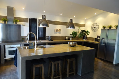 Cette image montre une grande cuisine design avec un évier encastré, un plan de travail en béton, une crédence beige, un sol en bois brun et îlot.