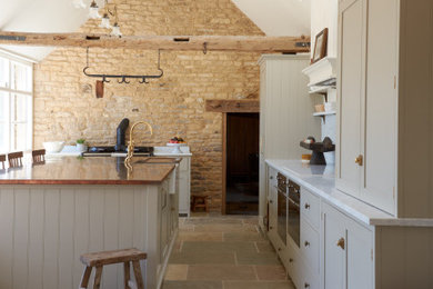 Large rustic kitchen/diner in Other with shaker cabinets, beige cabinets, marble worktops, limestone flooring, an island, multi-coloured floors, white worktops, exposed beams and a feature wall.
