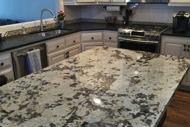 Photo of a traditional l-shaped kitchen in San Diego with an undermount sink, raised-panel cabinets, white cabinets, granite benchtops, glass tile splashback, bamboo floors, with island, brown floor and black benchtop.