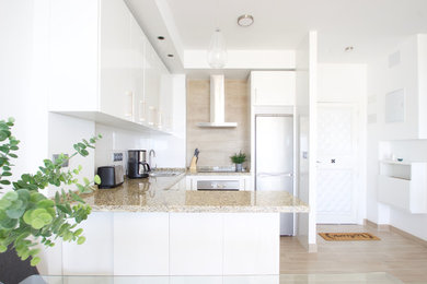Photo of a mid-sized scandinavian u-shaped kitchen in Malaga with a farmhouse sink, flat-panel cabinets, white cabinets, granite benchtops, stainless steel appliances, light hardwood floors, beige floor and beige benchtop.