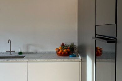 Diseño de cocinas en L minimalista de tamaño medio abierta con armarios con paneles lisos, puertas de armario blancas, encimera de mármol, suelo de madera clara y encimeras grises