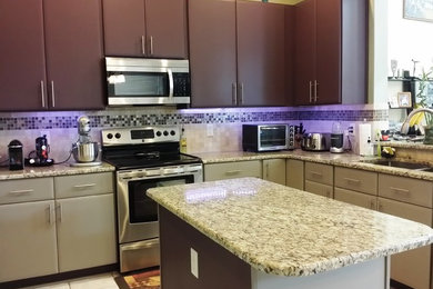 This is an example of a mid-sized contemporary l-shaped eat-in kitchen in Orlando with flat-panel cabinets, stainless steel appliances, with island, a double-bowl sink, grey cabinets, granite benchtops, white splashback, glass tile splashback and ceramic floors.