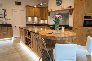 Design ideas for a large contemporary galley kitchen/diner in Other with a submerged sink, raised-panel cabinets, medium wood cabinets, granite worktops, ceramic splashback, black appliances, light hardwood flooring and a breakfast bar.
