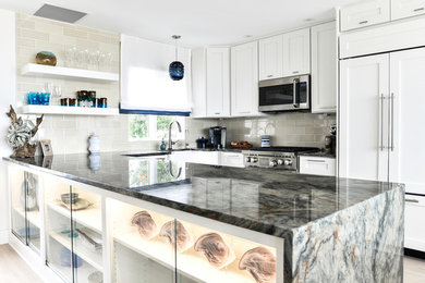 Inspiration for a mid-sized u-shaped kitchen pantry in Jacksonville with a farmhouse sink, recessed-panel cabinets, white cabinets, granite benchtops, beige splashback, subway tile splashback, stainless steel appliances, light hardwood floors, a peninsula, beige floor and grey benchtop.