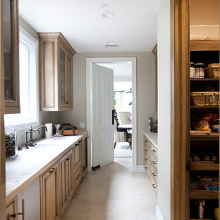 Réalisation d'une grande arrière-cuisine parallèle tradition avec un évier de ferme, un placard avec porte à panneau encastré, des portes de placard en bois vieilli, un plan de travail en calcaire, une crédence beige, une crédence en carrelage de pierre, un électroménager encastrable, un sol en calcaire, un sol beige et un plan de travail beige.