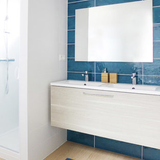 Cette image montre une salle de bain design de taille moyenne avec un placard à porte plane, des portes de placard en bois clair, une douche d'angle, un carrelage bleu, un mur blanc, un plan vasque, un sol marron et une cabine de douche à porte battante.