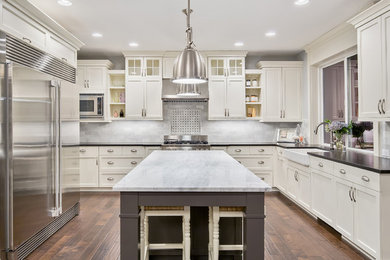 Transitional l-shaped dark wood floor and brown floor kitchen photo in Toronto with a farmhouse sink, shaker cabinets, beige cabinets, gray backsplash, stainless steel appliances, an island and black countertops