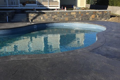 Example of a large trendy backyard stamped concrete and custom-shaped pool design in Portland Maine