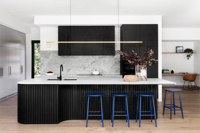 This is an example of a contemporary l-shaped open plan kitchen in Melbourne with an undermount sink, flat-panel cabinets, grey splashback, stone slab splashback, black appliances, medium hardwood floors, with island, brown floor and white benchtop.