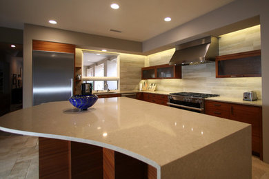 This is an example of a large contemporary l-shaped eat-in kitchen in Phoenix with a single-bowl sink, flat-panel cabinets, medium wood cabinets, solid surface benchtops, beige splashback, porcelain splashback, limestone floors, with island and stainless steel appliances.