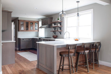 Mid-sized transitional galley eat-in kitchen in Burlington with a farmhouse sink, flat-panel cabinets, grey cabinets, quartz benchtops, white splashback, subway tile splashback, stainless steel appliances, medium hardwood floors, a peninsula and brown floor.