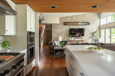 This is an example of a mid-sized transitional l-shaped open plan kitchen in Nashville with an undermount sink, recessed-panel cabinets, white cabinets, quartz benchtops, grey splashback, ceramic splashback, stainless steel appliances, medium hardwood floors, with island, brown floor, white benchtop and wood.