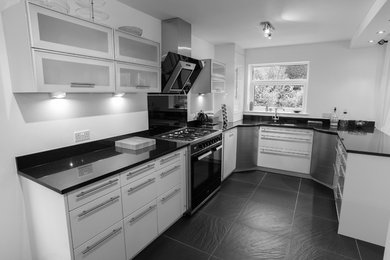 Ejemplo de cocina moderna de tamaño medio sin isla con fregadero integrado, armarios con paneles lisos, puertas de armario blancas, encimera de granito, electrodomésticos negros y suelo de pizarra