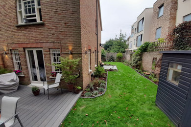 This is an example of a medium sized contemporary back partial sun garden wall in London with a flowerbed and decking.