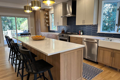 Inspiration for a large farmhouse l-shaped light wood floor eat-in kitchen remodel in Boston with a farmhouse sink, shaker cabinets, light wood cabinets, quartz countertops, blue backsplash, cement tile backsplash, stainless steel appliances, an island and white countertops