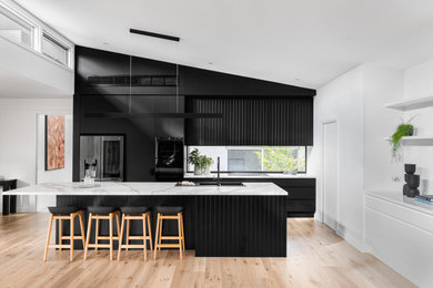Photo of a large contemporary kitchen in Melbourne with a drop-in sink, black cabinets, marble benchtops, glass sheet splashback, black appliances, light hardwood floors and with island.