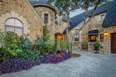 Example of a huge tuscan beige two-story stone house exterior design in Austin with a shingle roof and a shed roof