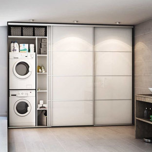 Photo of a medium sized mediterranean single-wall separated utility room in Florence with a submerged sink, glass-front cabinets, white cabinets, glass worktops, beige walls, ceramic flooring, a stacked washer and dryer and beige floors.