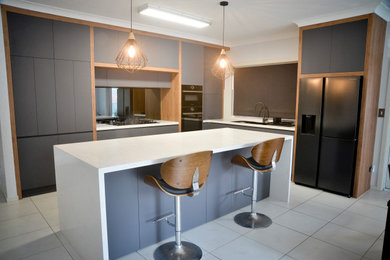 Design ideas for a mid-sized modern l-shaped open plan kitchen in Sydney with a drop-in sink, flat-panel cabinets, grey cabinets, quartz benchtops, multi-coloured splashback, mirror splashback, black appliances, porcelain floors, with island, yellow floor and white benchtop.
