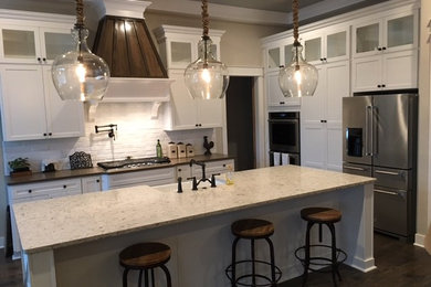 Kitchen - large transitional l-shaped dark wood floor kitchen idea in Columbus with a farmhouse sink, shaker cabinets, white cabinets, quartzite countertops, white backsplash, brick backsplash, stainless steel appliances and an island