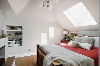 Modelo de dormitorio principal y abovedado de tamaño medio con paredes blancas, suelo de madera en tonos medios, todas las chimeneas y suelo marrón